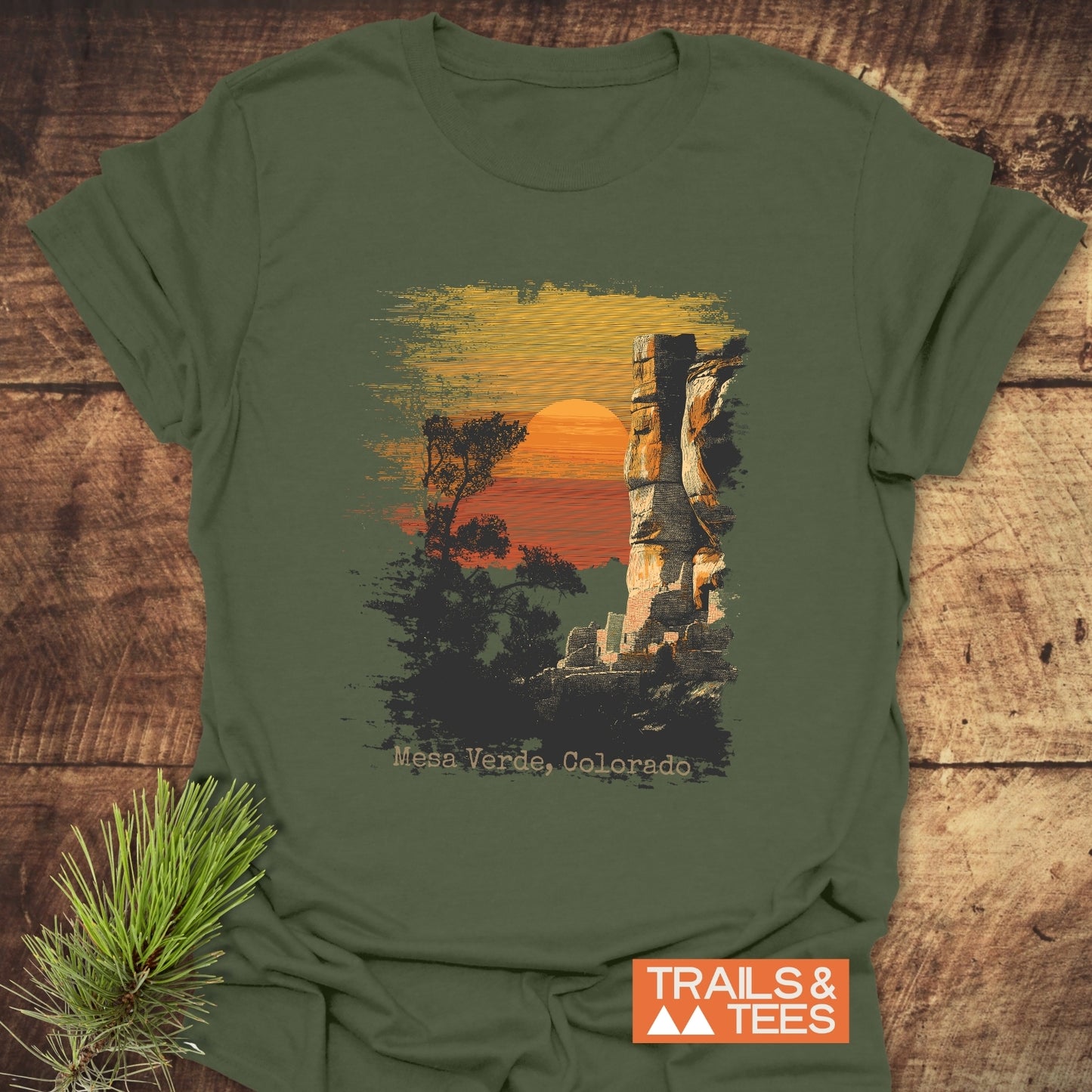 Mesa Verde, Colorado T-Shirt featuring a sunset scene with trees and cliffs, crafted from soft cotton, offering comfort and durability with a Trails & Tees logo.
