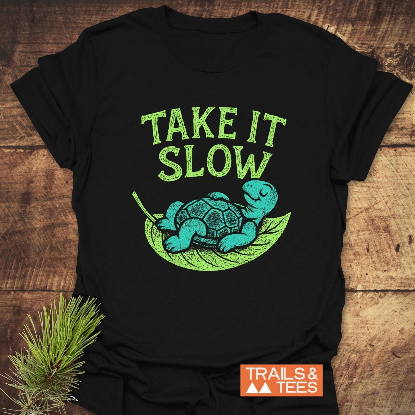 Take It Slow T-Shirt: Features a relaxed turtle on a leaf hammock with TAKE IT SLOW above. Includes Trails & Tees logo, promising comfort and durability.