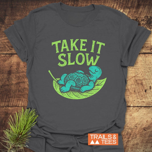 Take It Slow T-Shirt with turquoise turtle on leaf, TAKE IT SLOW text, and TRAILS & TEES logo. Soft, durable, and adventure-ready design.