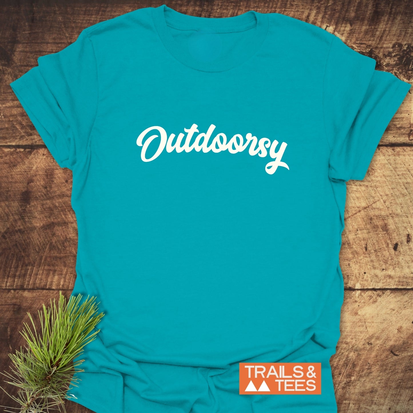 Outdoorsy T-Shirt with Outdoorsy in white script across the chest, featuring an orange Trails & Tees logo, complemented by a pine sprig.