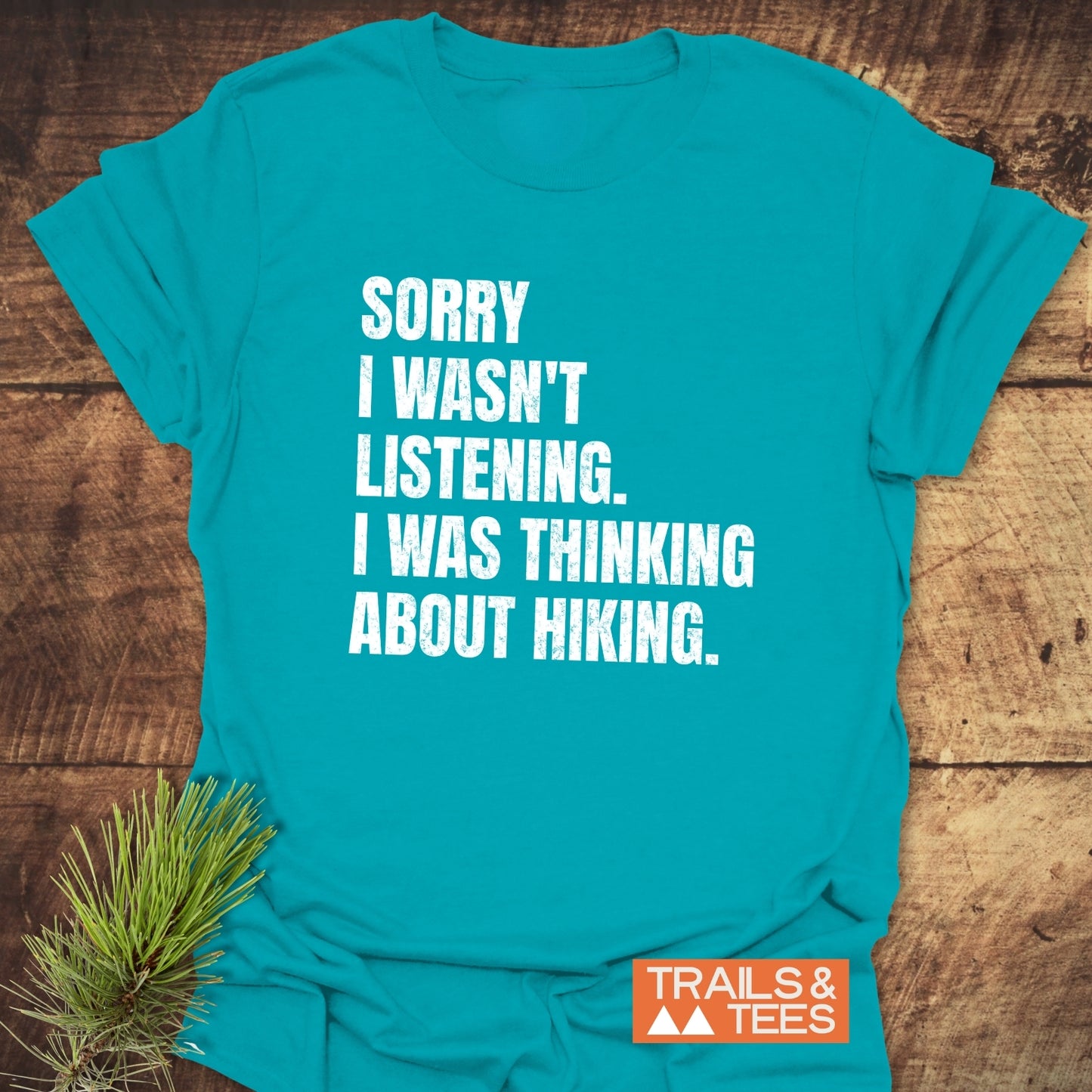 Sorry I Wasn't Listening Hiking T-Shirt with white distressed text on turquoise. Features include soft ring-spun cotton, pre-shrunk fit, durable prints, and eco-friendly production.