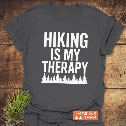 Hiking Is My Therapy T-Shirt on wooden surface, features bold text and tree silhouettes; made of ring-spun cotton for comfort and durability.