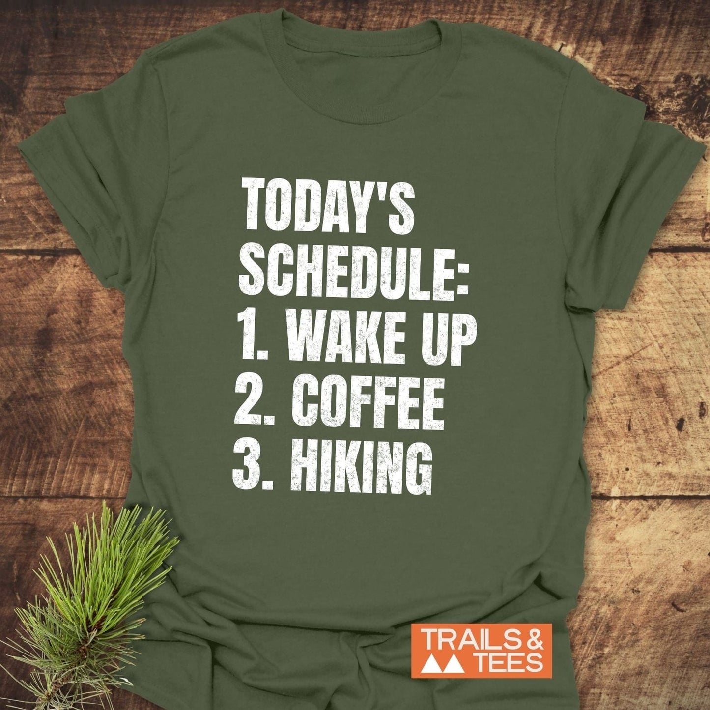 Today's Schedule Hiking T-Shirt with distressed lettering, featuring a pine needle accent and Trails & Tees branding, embodying outdoor adventure and comfort.