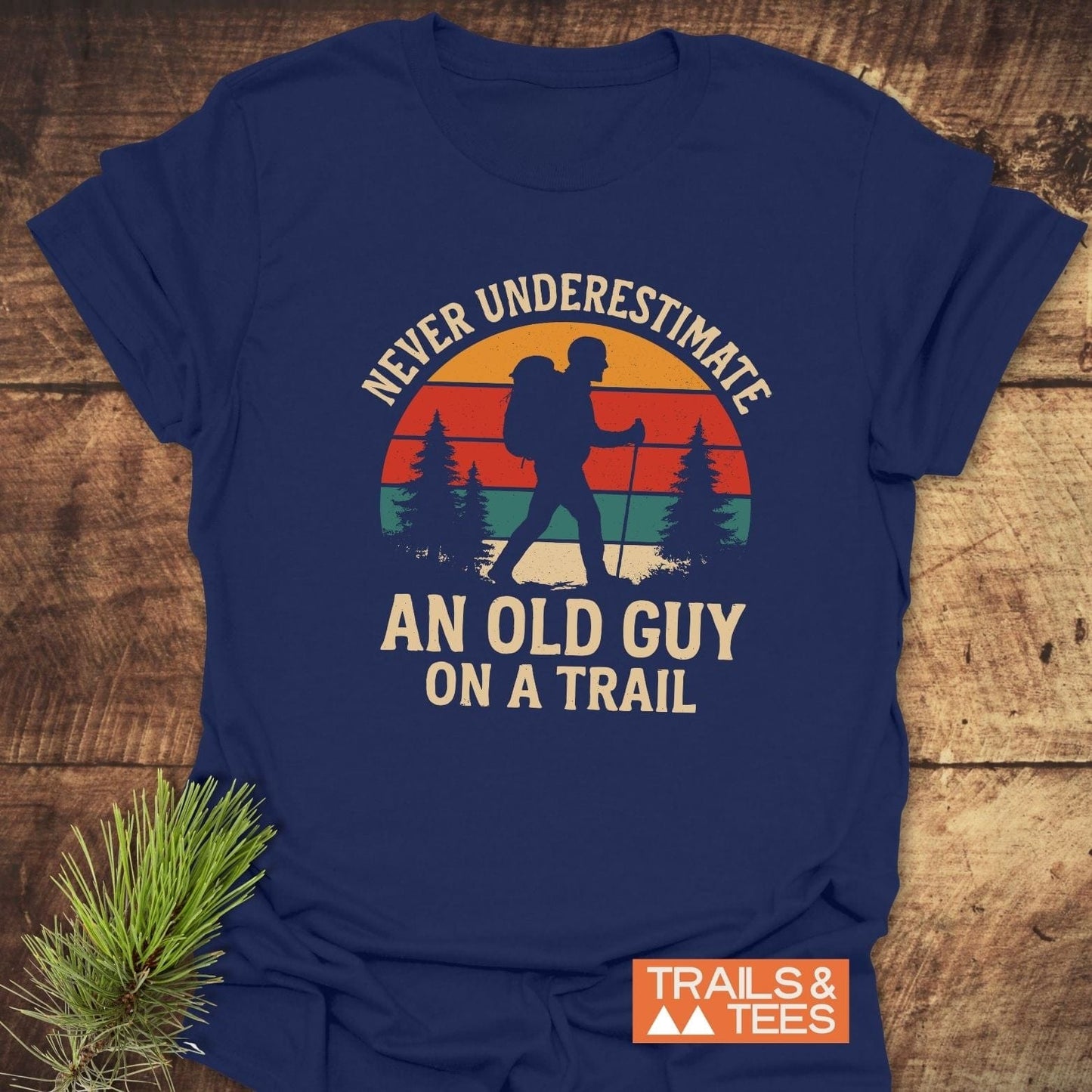 Never Underestimate T-Shirt features a hiker silhouette with a sunset backdrop on navy fabric, highlighting trail-tested comfort and durable prints.