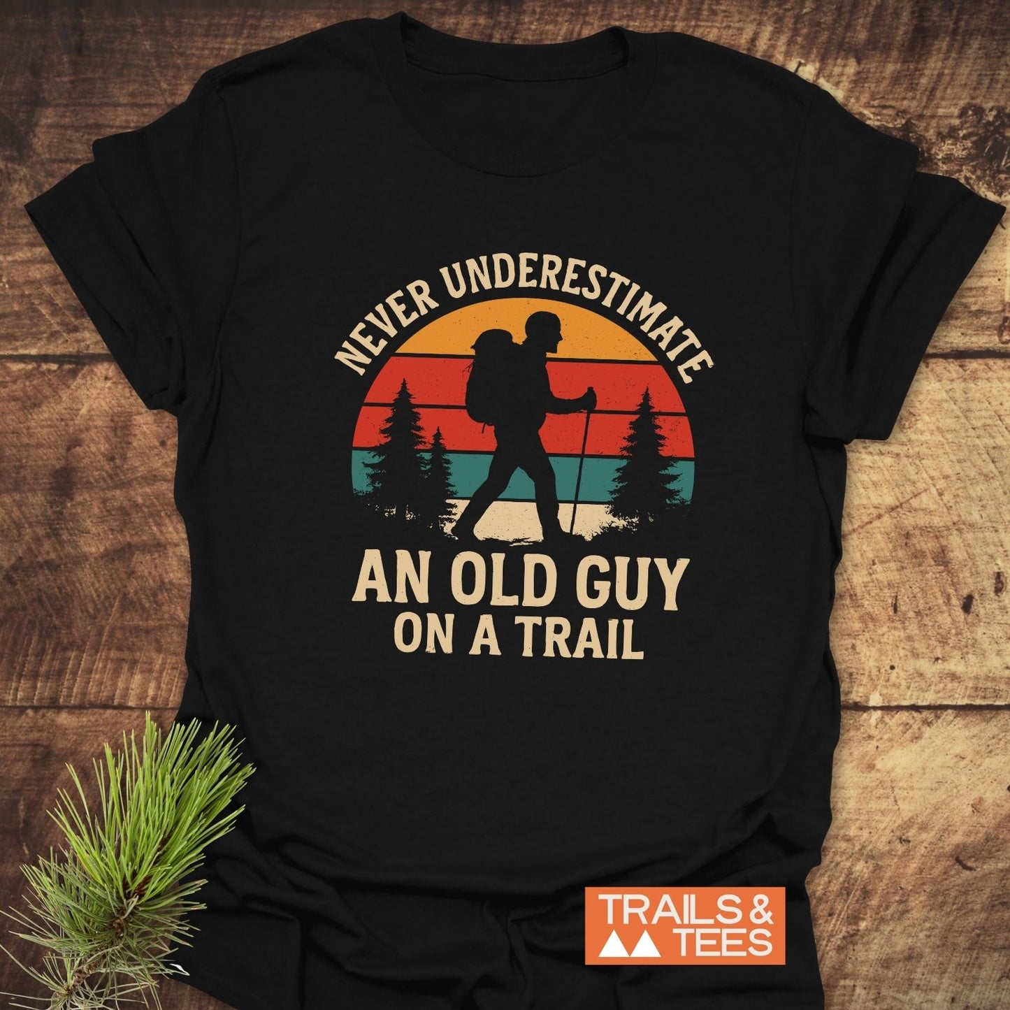Never Underestimate T-Shirt featuring a retro hiker graphic with pine trees and sunset backdrop, designed for comfort and durability with ring-spun cotton.