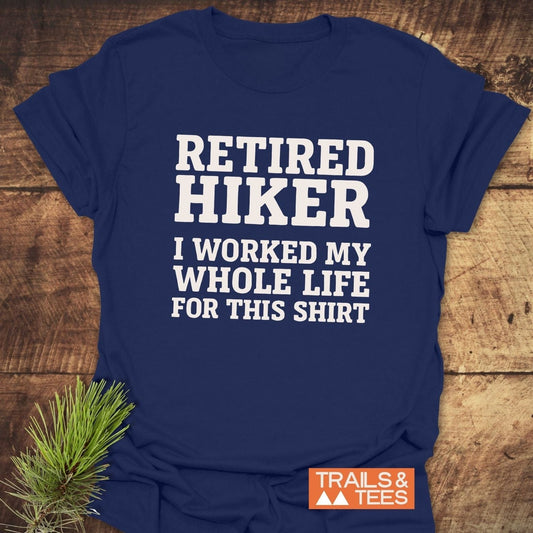 Navy blue Retired Hiker T-shirt with bold white text, laid flat with a pine sprig, featuring TRAILS & TEES logo, emphasizing comfort and durability.