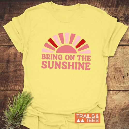 Bring On The Sunshine T-Shirt featuring a half-sun graphic and bold text, laid flat with a Trails & Tees logo, showcasing outdoor-inspired comfort and durability.