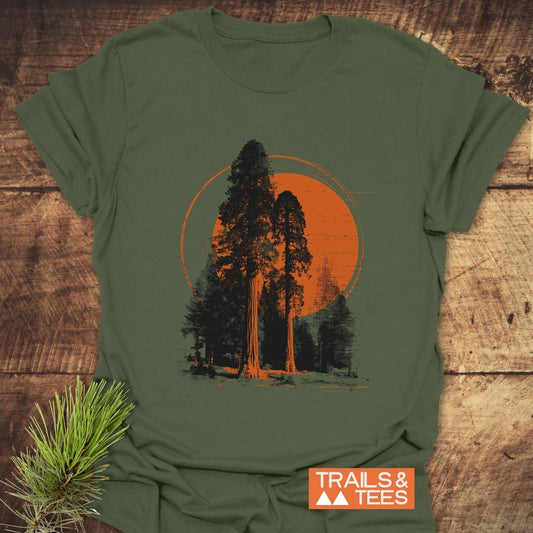 Sequoia T-Shirt with forest print, featuring black trees and orange sun. Laid on wood, includes TRAILS & TEES badge. Ideal for outdoor enthusiasts.