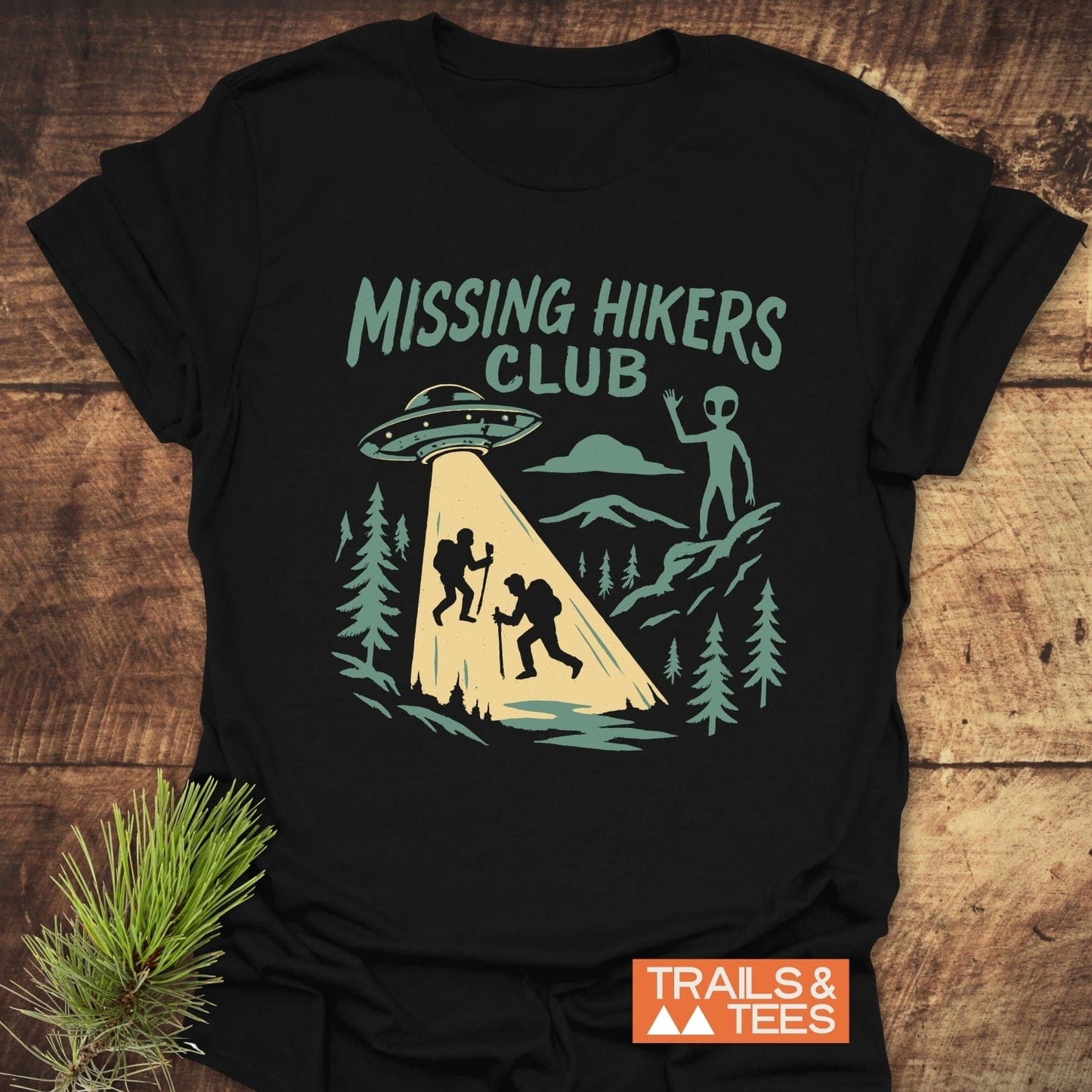 Missing Hikers Club T-Shirt with a graphic of hikers and a UFO, crafted from soft ring-spun cotton, ideal for outdoor enthusiasts.