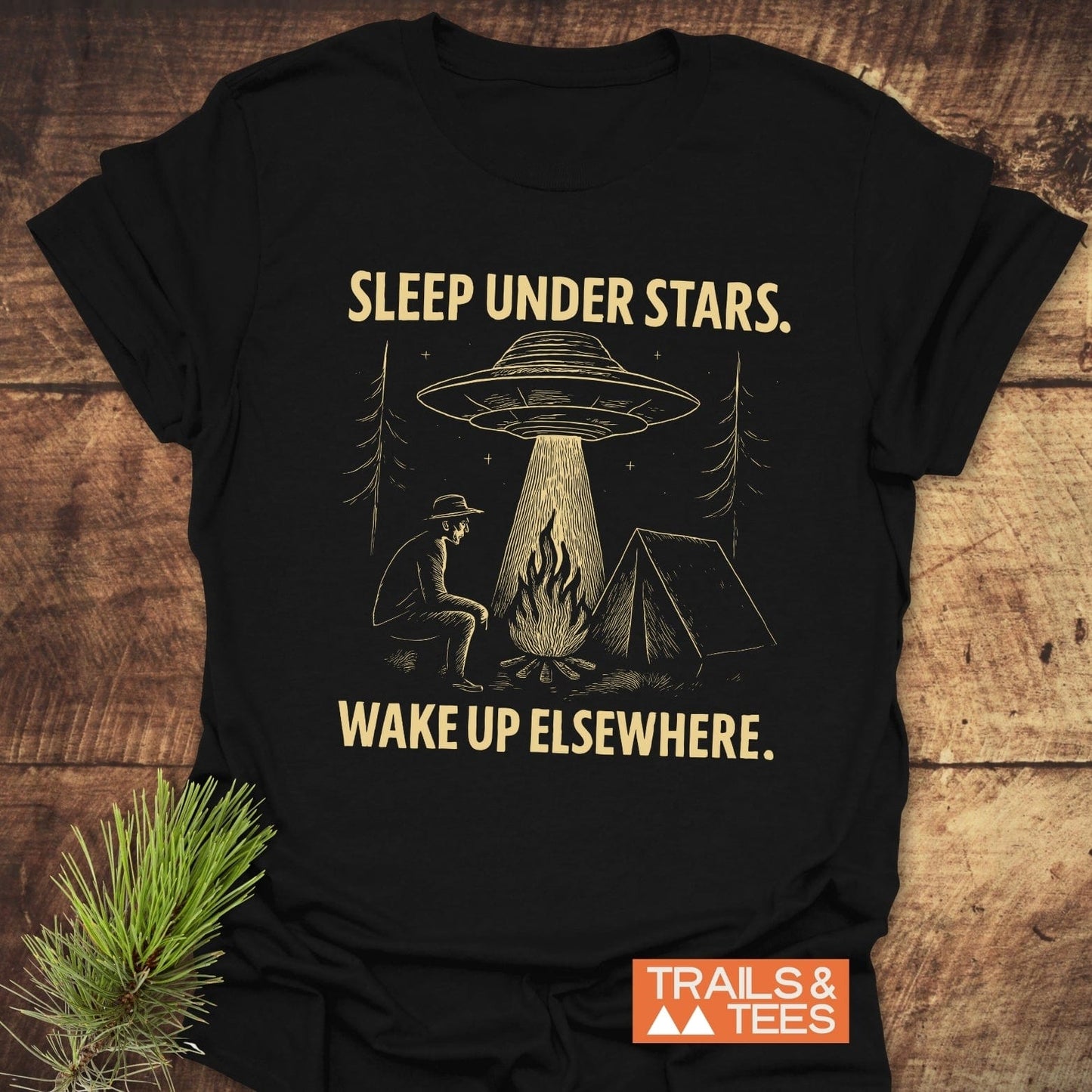 Sleep Under Stars UFO T-Shirt featuring a camping scene with a UFO, pine trees, and bold text. Made from soft, durable cotton for outdoor enthusiasts.