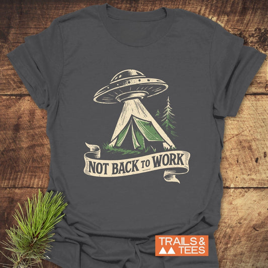 Charcoal-gray T-shirt featuring a flying saucer graphic and Not Back To Work banner, styled with a pine sprig on a wooden surface.