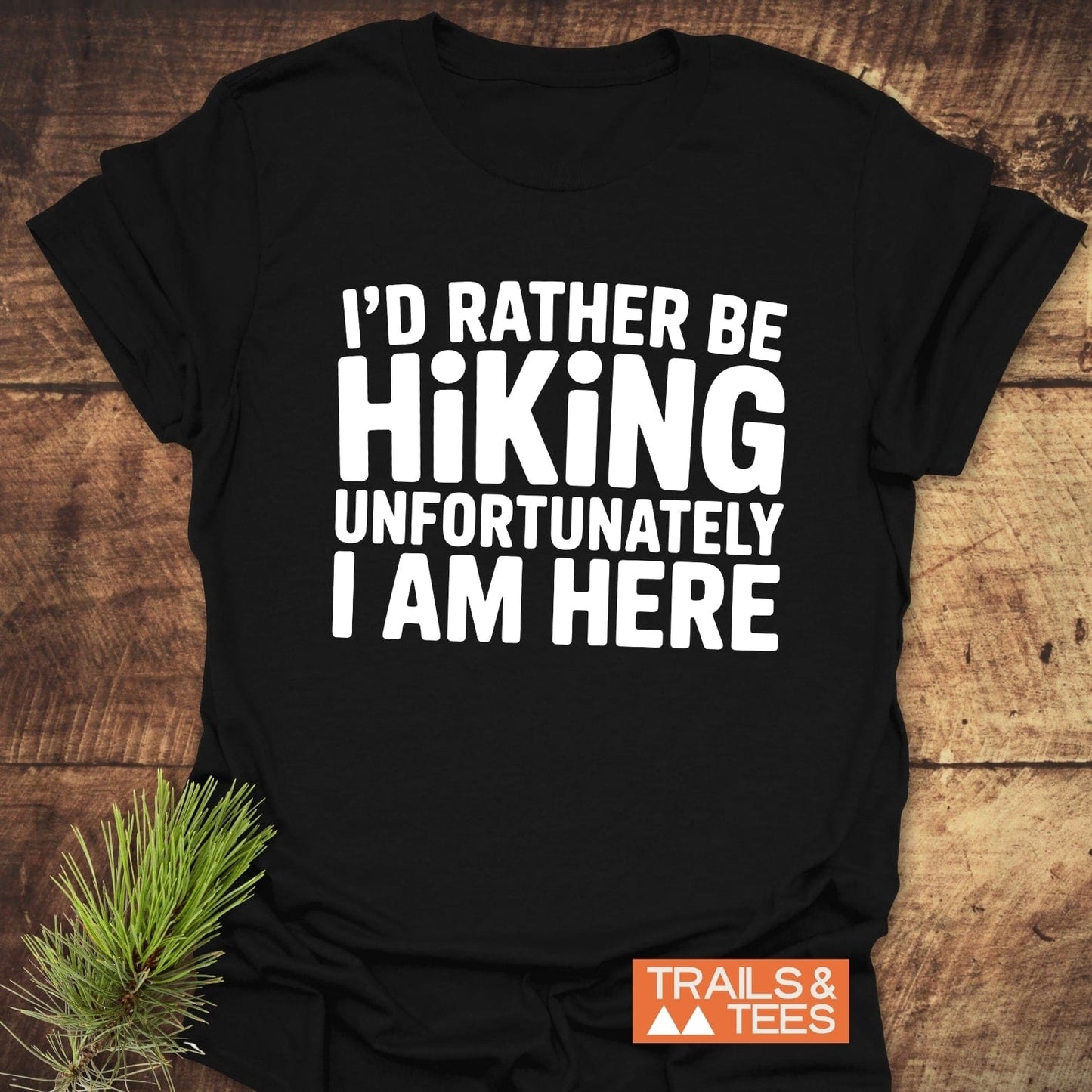 I'd Rather Be Hiking... T-Shirt on rustic wood with Trails & Tees logo, featuring bold white lettering, crafted from soft cotton for lasting comfort.