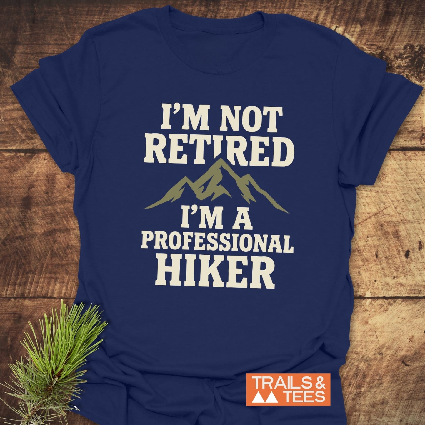 Navy T-shirt with I'M NOT RETIRED, I'M A PROFESSIONAL HIKER slogan and mountain graphic; TRAILS & TEES logo, crafted for outdoor enthusiasts.