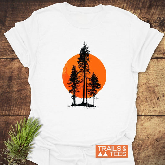 Sunset Trees T-Shirt featuring black pine-tree silhouettes on an orange circle, styled with a pine branch. Soft, durable, and perfect for outdoor enthusiasts.