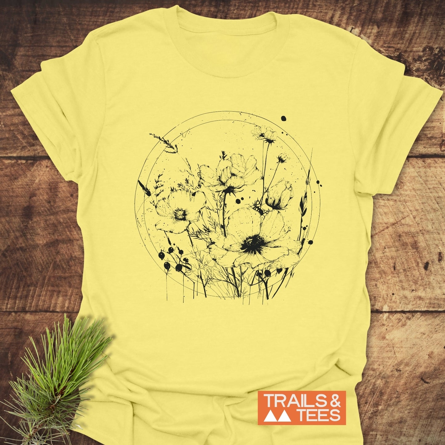 Wildflower Circle T-Shirt featuring a black wildflower illustration on pale yellow fabric, styled on wood. Made from soft cotton, perfect for outdoor enthusiasts.