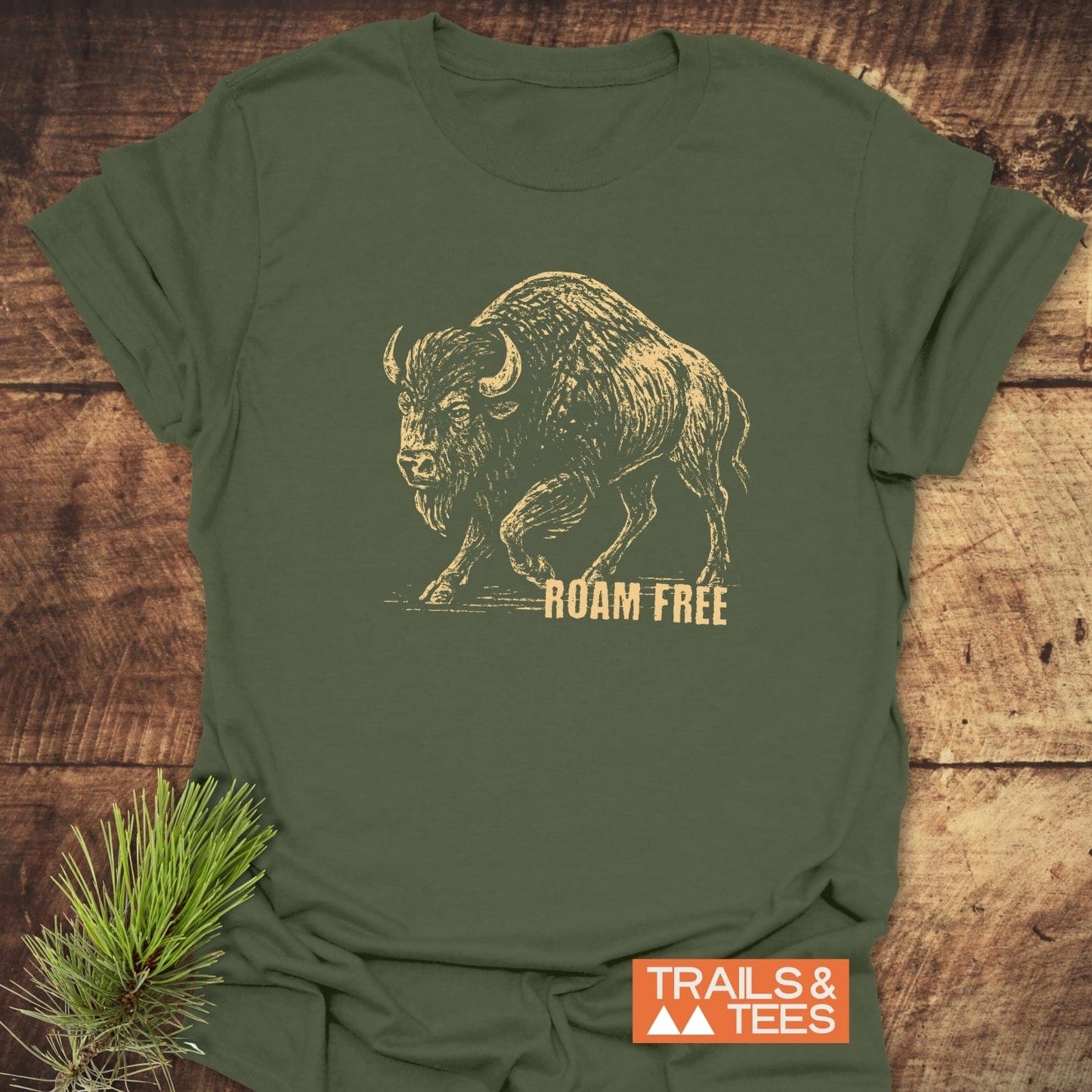 Roaming Bison T-Shirt on wood surface, featuring a vintage bison sketch with “ROAM FREE” slogan; orange “TRAILS & TEES” logo, embodying adventure-ready comfort.