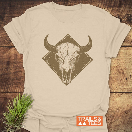 Bison Skull Western T-Shirt flat-lay, featuring a distressed horned skull design; styled with a pine sprig and TRAILS & TEES logo in orange.