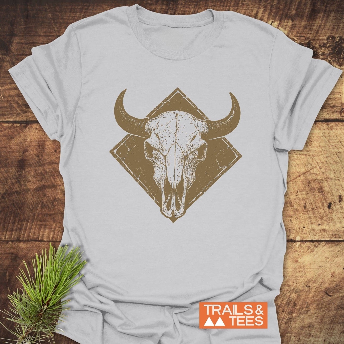 Bison Skull Western T-Shirt featuring a distressed bovine skull graphic on soft, lightweight cotton, emphasizing outdoor spirit and comfort. Includes TRAILS & TEES logo and pine sprig accent.