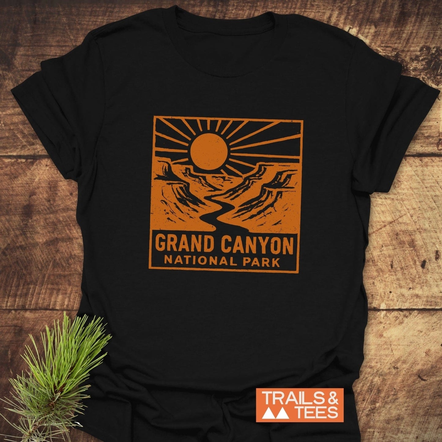 Grand Canyon NP T-Shirt with an orange canyon scene design. Features TRAILS & TEES logo. Made of soft ring-spun cotton, pre-shrunk, durable print.