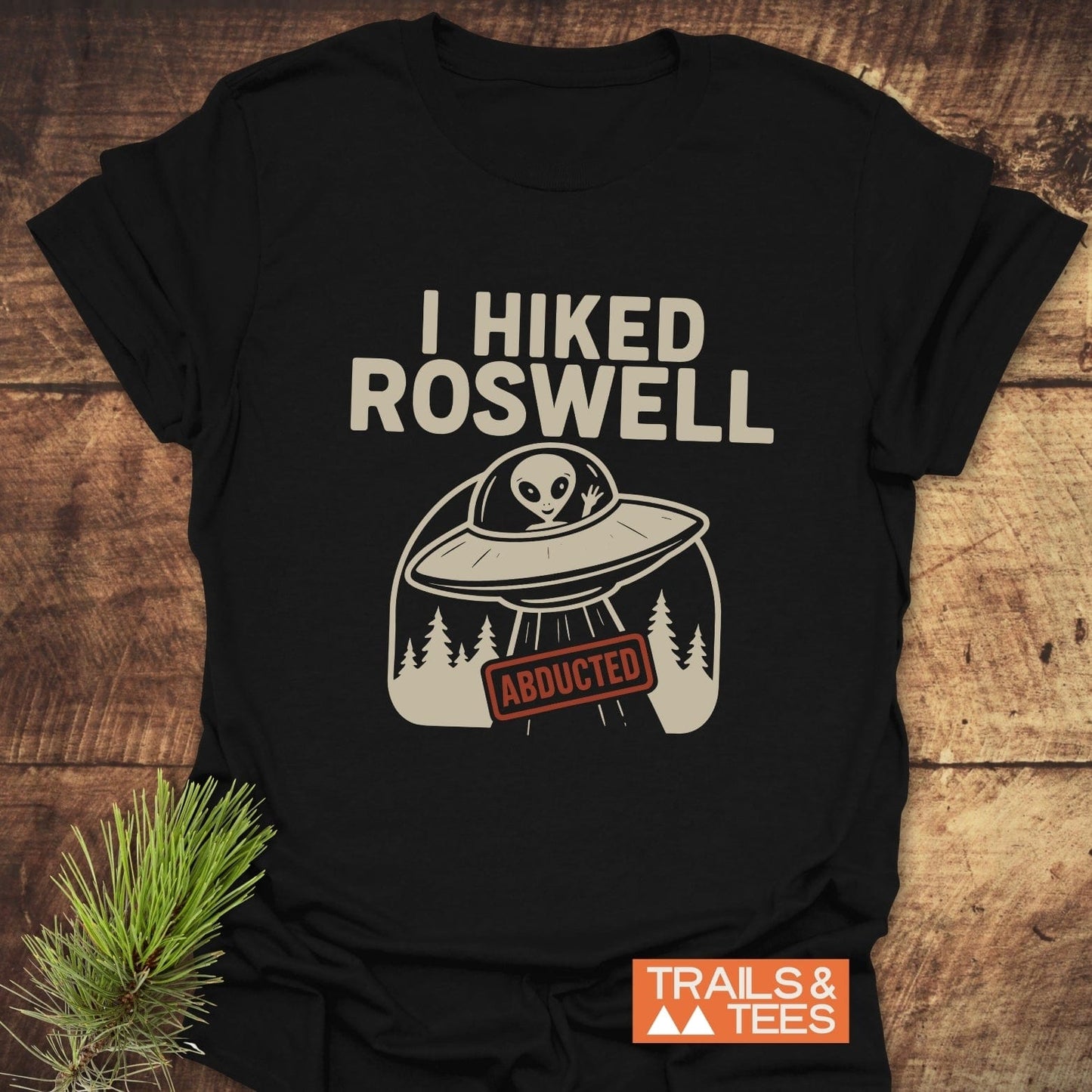 I Hiked Roswell T-Shirt featuring a UFO graphic with an alien and ABDUCTED sign, crafted from soft cotton for comfort, includes Trails & Tees logo.