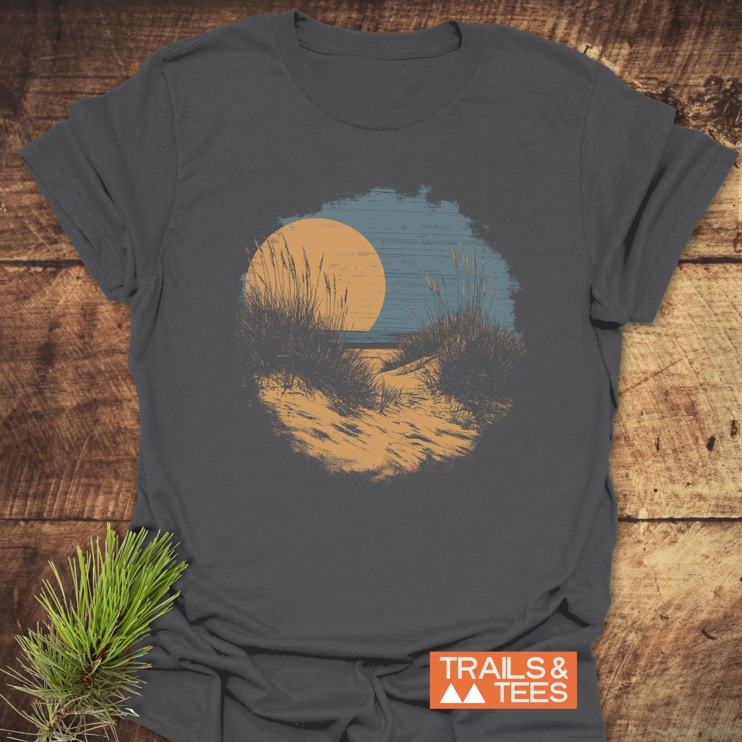 Indiana Dunes National Park T-Shirt on rustic wood, featuring a scenic dune path graphic under an orange sun. Includes a TRAILS & TEES logo and pine needle accent.