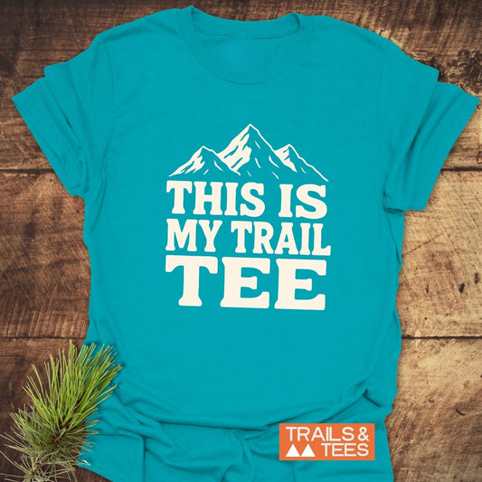 This Is My Trail Tee T-Shirt with mountain graphic and ‘THIS IS MY TRAIL TEE’ text, showcasing comfort-focused design for outdoor enthusiasts, laid flat with pine needles.