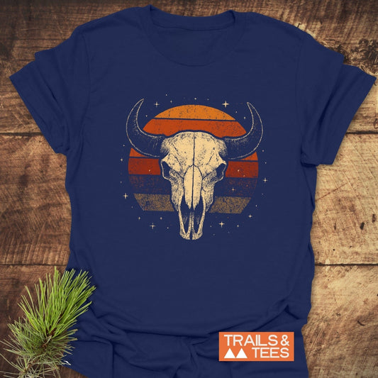 Retro Buffalo Skull T-Shirt featuring a weathered skull over a retro sunset circle with stars, orange “TRAILS & TEES” label, styled with a pine sprig.