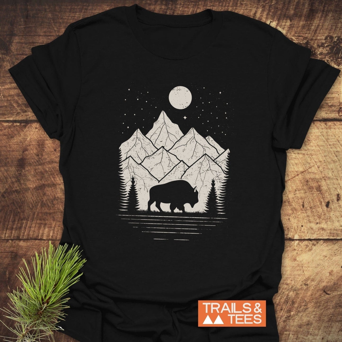 Nightsky Buffalo T-Shirt features a mountain and bison graphic, emphasizing outdoor adventure. Made from soft cotton, it highlights Trails & Tees' commitment to comfort.