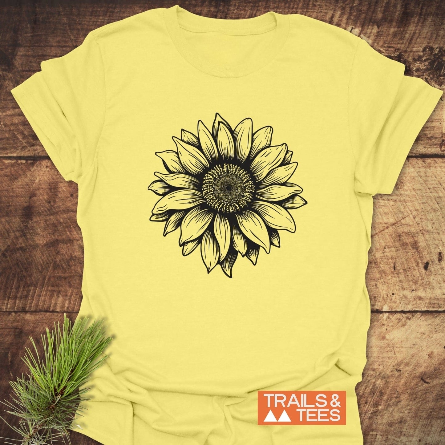 Sunflower T-Shirt on wood, features a black sunflower illustration, Trails & Tees logo. Crafted from soft ring-spun cotton for adventure-ready comfort.