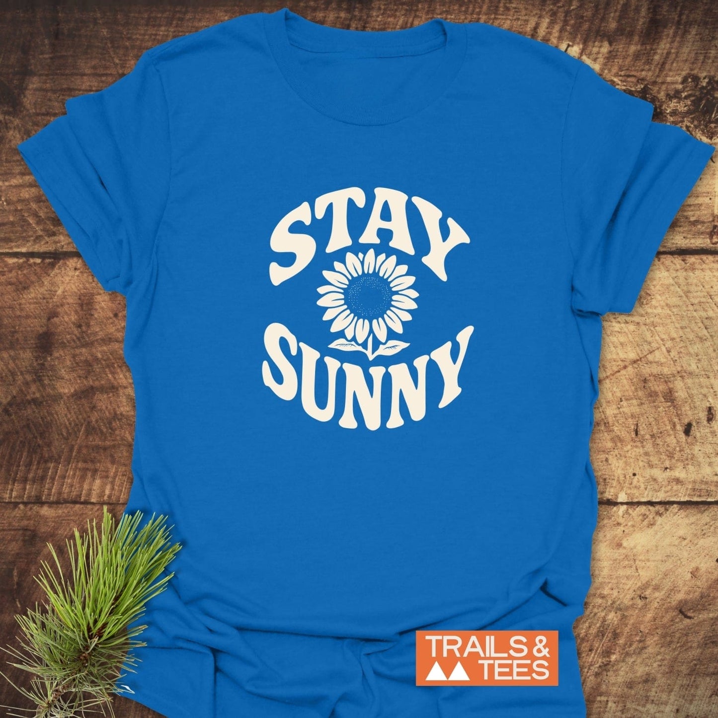 Stay Sunny T-Shirt featuring a white sunflower graphic and text on soft, lightweight cotton, ideal for outdoor adventures. Includes Trails & Tees brand logo.