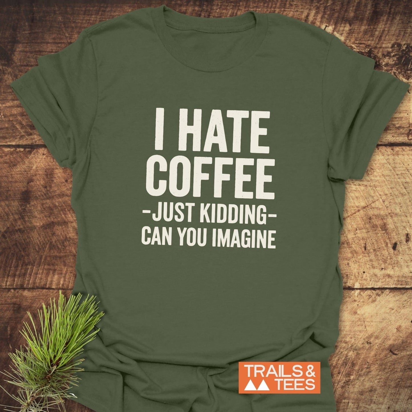 Olive-green I Hate Coffee T-shirt featuring bold white slogan, crafted from soft ring-spun cotton, laid flat with Trails & Tees logo on rustic wood surface.