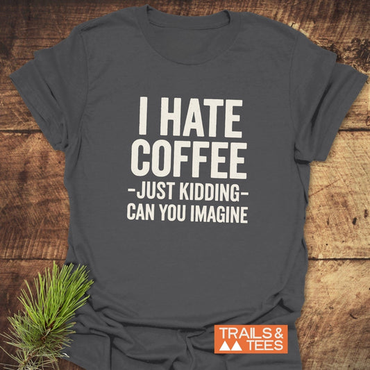 Charcoal-gray I Hate Coffee T-shirt with white slogan, flat-laid on wood. Features pine sprig and TRAILS & TEES label, embodying outdoor adventure comfort.