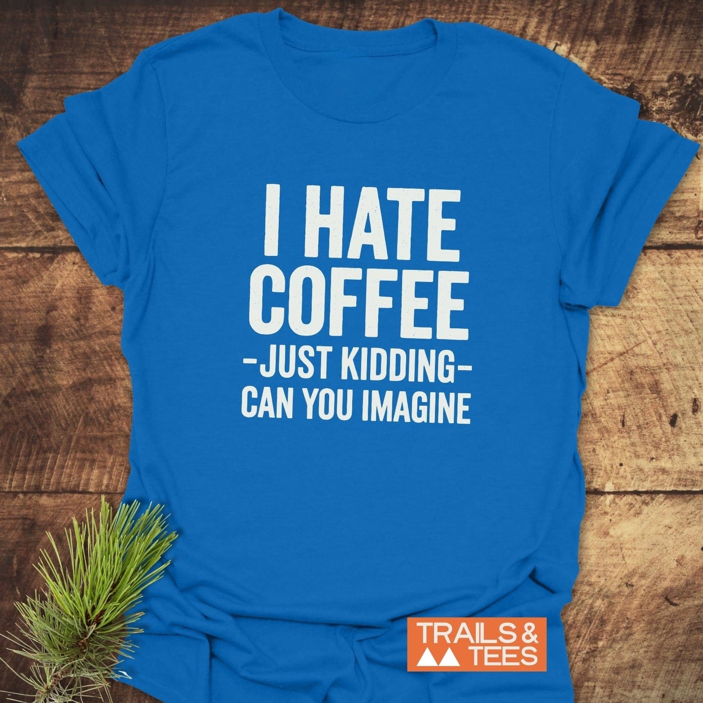 Bright blue I Hate Coffee T-shirt with white slogan, laid flat. Features durable DTF print, Trails & Tees logo, and pine sprig accent.