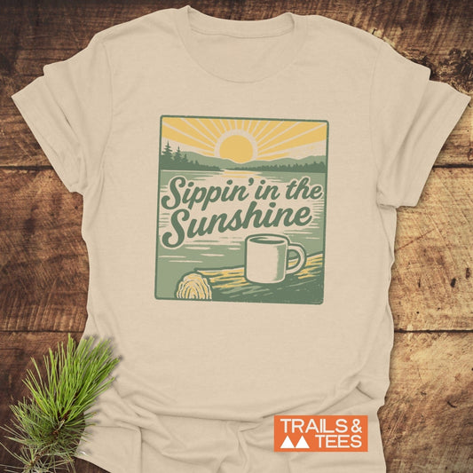 Sippin' In The Sunshine T-Shirt featuring a vintage sunlit lake scene with a coffee mug, showcasing Trails & Tees' rustic, adventure-ready design.