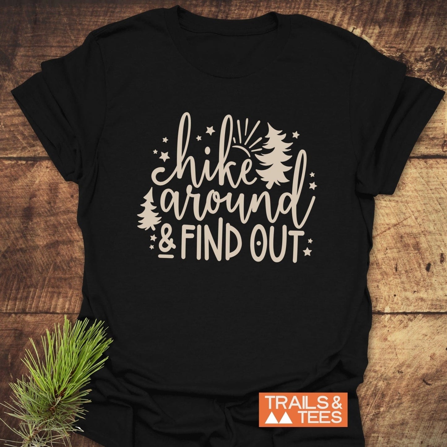 Black T-shirt with Hike Around & Find Out design featuring pine trees and stars, orange TRAILS & TEES logo, emphasizing outdoor adventure and comfort.
