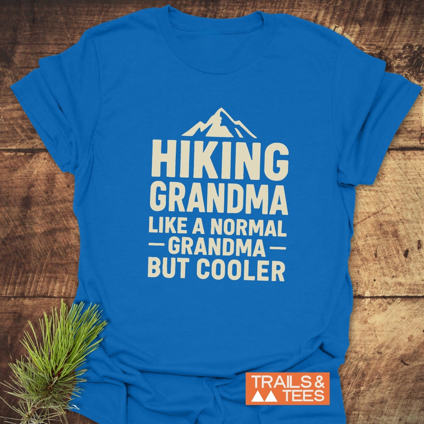 Bright blue Hiking Grandma T-shirt with mountain silhouette and bold white text, highlighting comfort and durable design. Includes Trails & Tees logo.