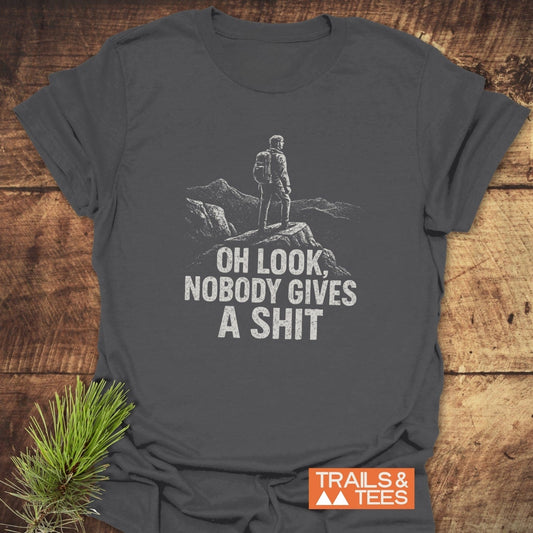 Dark-gray Oh Look! T-Shirt with a hiker graphic, mountain backdrop, and humorous text, featuring durable prints and a Trails & Tees logo.