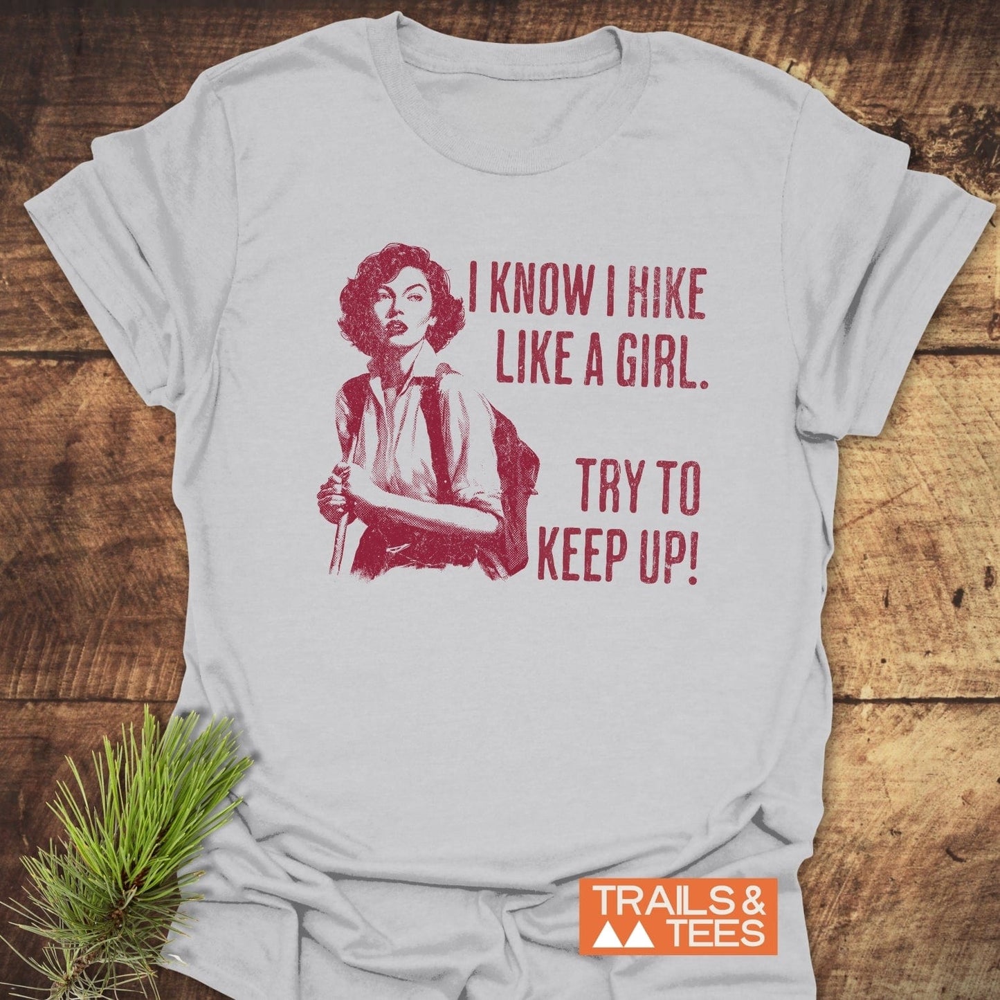 Hike Like A Girl T-Shirt with vintage hiker illustration and slogan in red. Soft ring-spun cotton, durable print, Trails & Tees logo included.