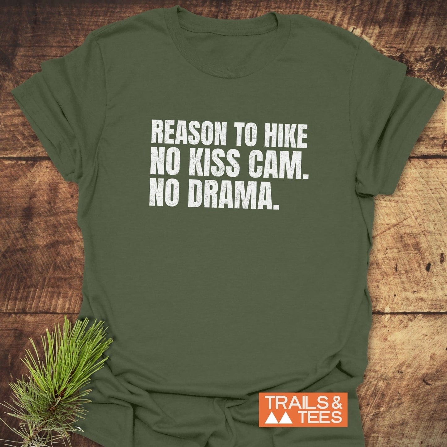 Reason To Hike: No Kiss Cam T-Shirt on wooden surface with bold white text. Features durable, comfortable ring-spun cotton, pre-shrunk, and eco-friendly prints.