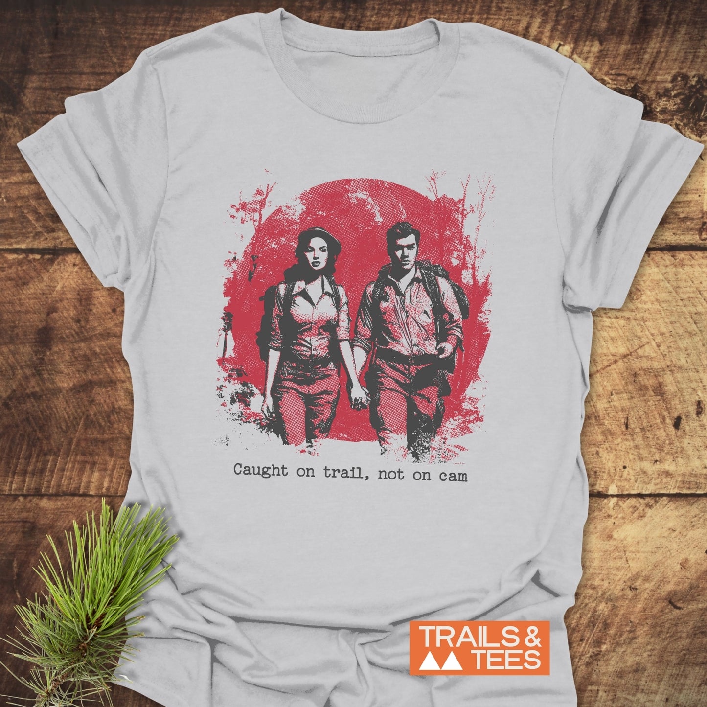 No Kiss Cam T-Shirt featuring a hiking couple graphic and slogan, laid on wood. Made from soft ring-spun cotton, perfect for outdoor enthusiasts.
