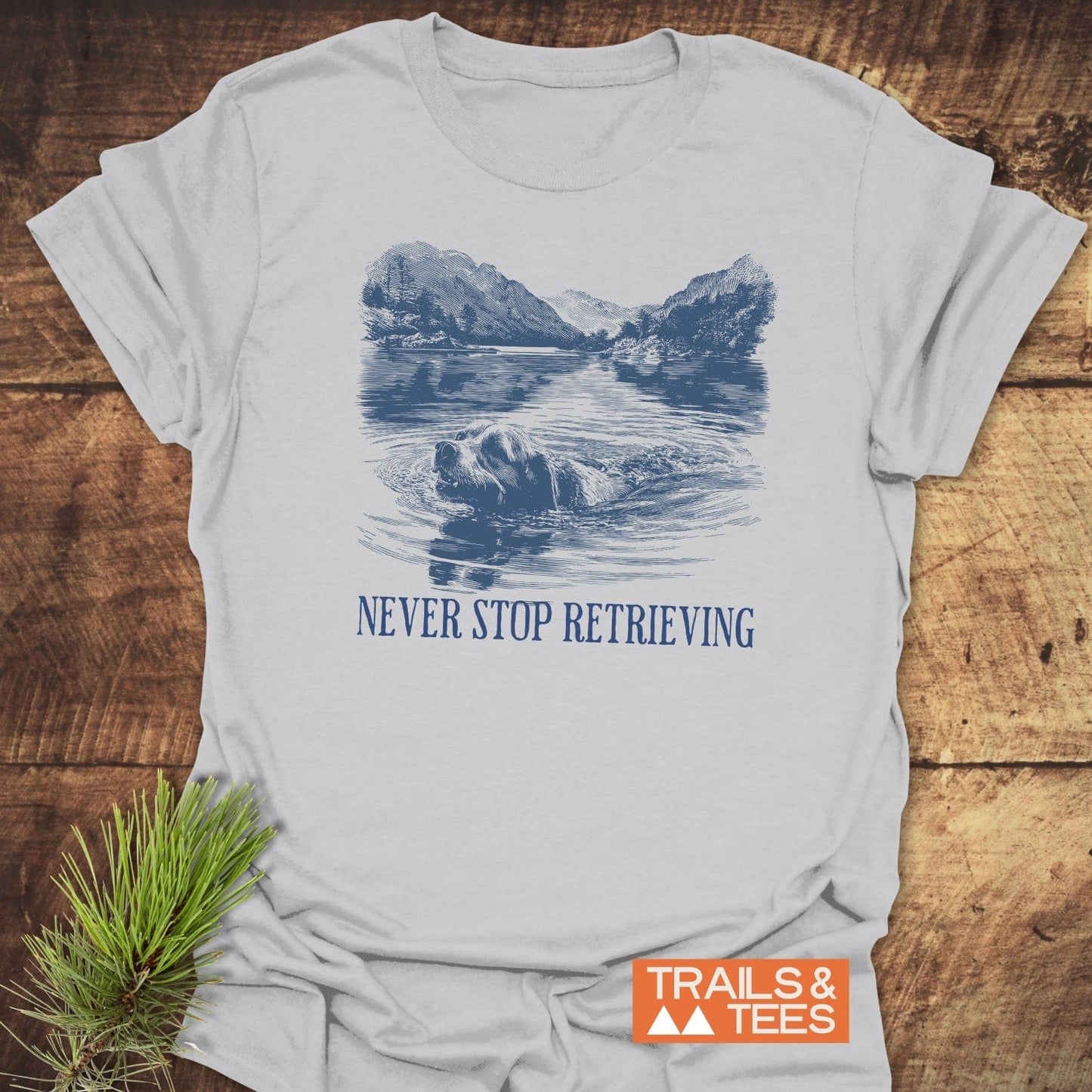 Never Stop... Golden Retriever T-Shirt features a retriever in a lake scene with NEVER STOP RETRIEVING slogan, ideal for outdoor enthusiasts.