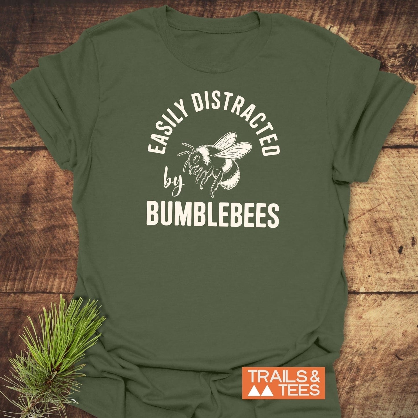 Easily Distracted By Bumblebees T-Shirt: Olive-green tee with bumblebee graphic and slogan, crafted from soft cotton for comfort and durability, logo and pine sprig included.