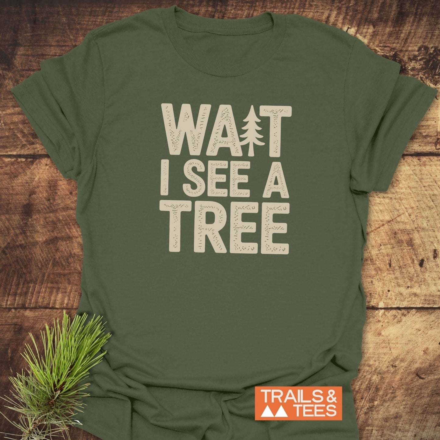 Wait I See A Tree T-Shirt flat-lay featuring off-white text and pine-tree icon on olive-green fabric, highlighting outdoor-themed design and durable, lightweight comfort.