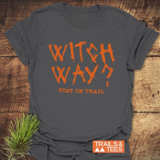 Witch Way? T-Shirt on rustic wood, featuring orange brush-style lettering. Made from soft cotton for comfort, with durable prints. Includes Trails & Tees logo.