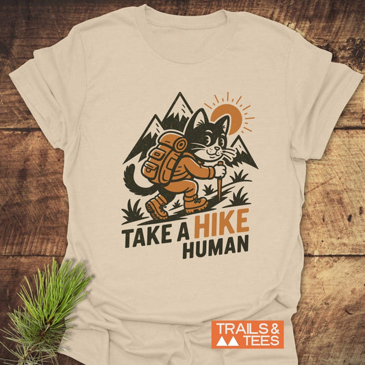 Take A Hike Human T-Shirt featuring a cartoon hiking cat, durable print, and comfortable ring-spun cotton, ideal for outdoor enthusiasts. Logo: Trails & Tees.