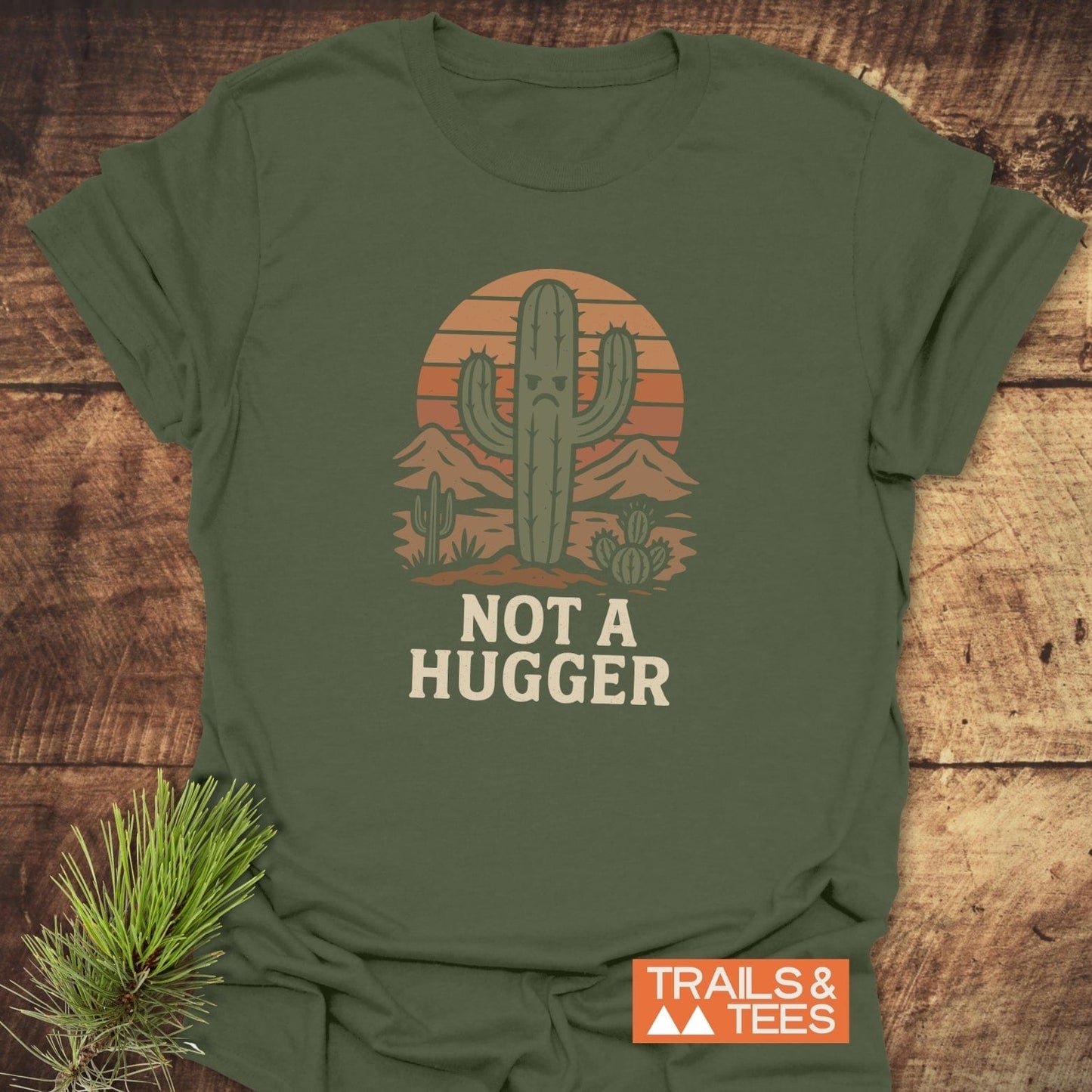 Not A Hugger T-Shirt with cactus and sunset design, featuring “NOT A HUGGER” text. Made of soft, durable cotton, ideal for outdoor enthusiasts.