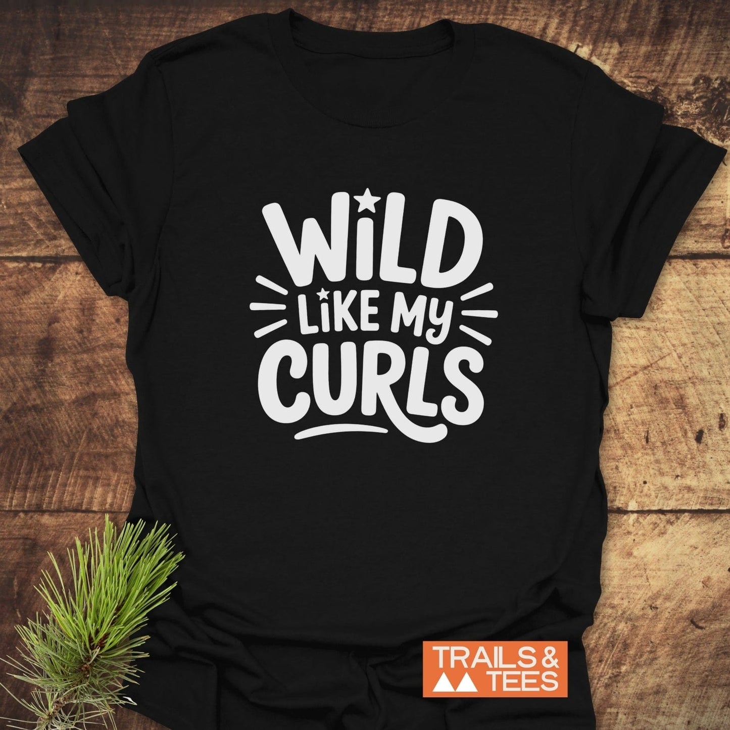 Wild Like My Curls T-Shirt on rustic wood, featuring bold white graphic with stars. Includes durable prints, taped shoulders, and is crafted for outdoor adventures.
