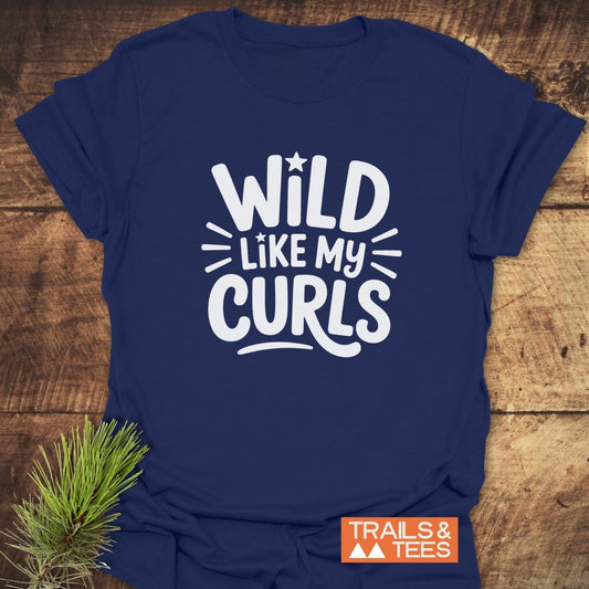 Navy-blue Wild Like My Curls T-shirt with playful lettering, featuring durable print, taped shoulders, and pre-shrunk fit. Includes Trails & Tees logo and pine sprig accent.