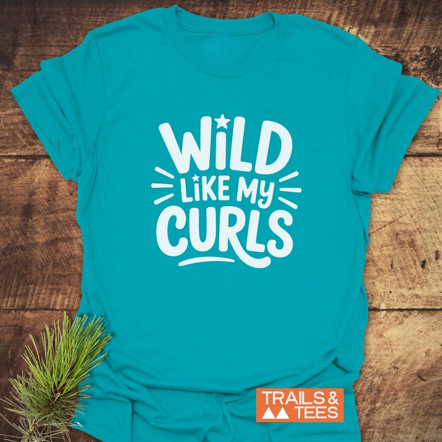 Teal T-shirt reading WILD LIKE MY CURLS in white, with playful accents. Features durable print, pre-shrunk cotton, taped shoulders. Branded TRAILS & TEES.