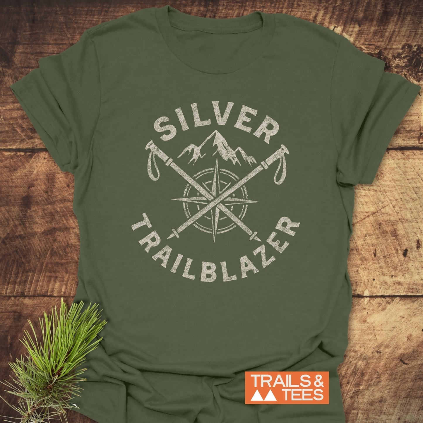 Silver Trailblazer T-Shirt with crossed ice-axes, compass rose, and mountain graphic. Crafted from soft cotton, perfect for outdoor enthusiasts. Includes TRAILS & TEES logo.